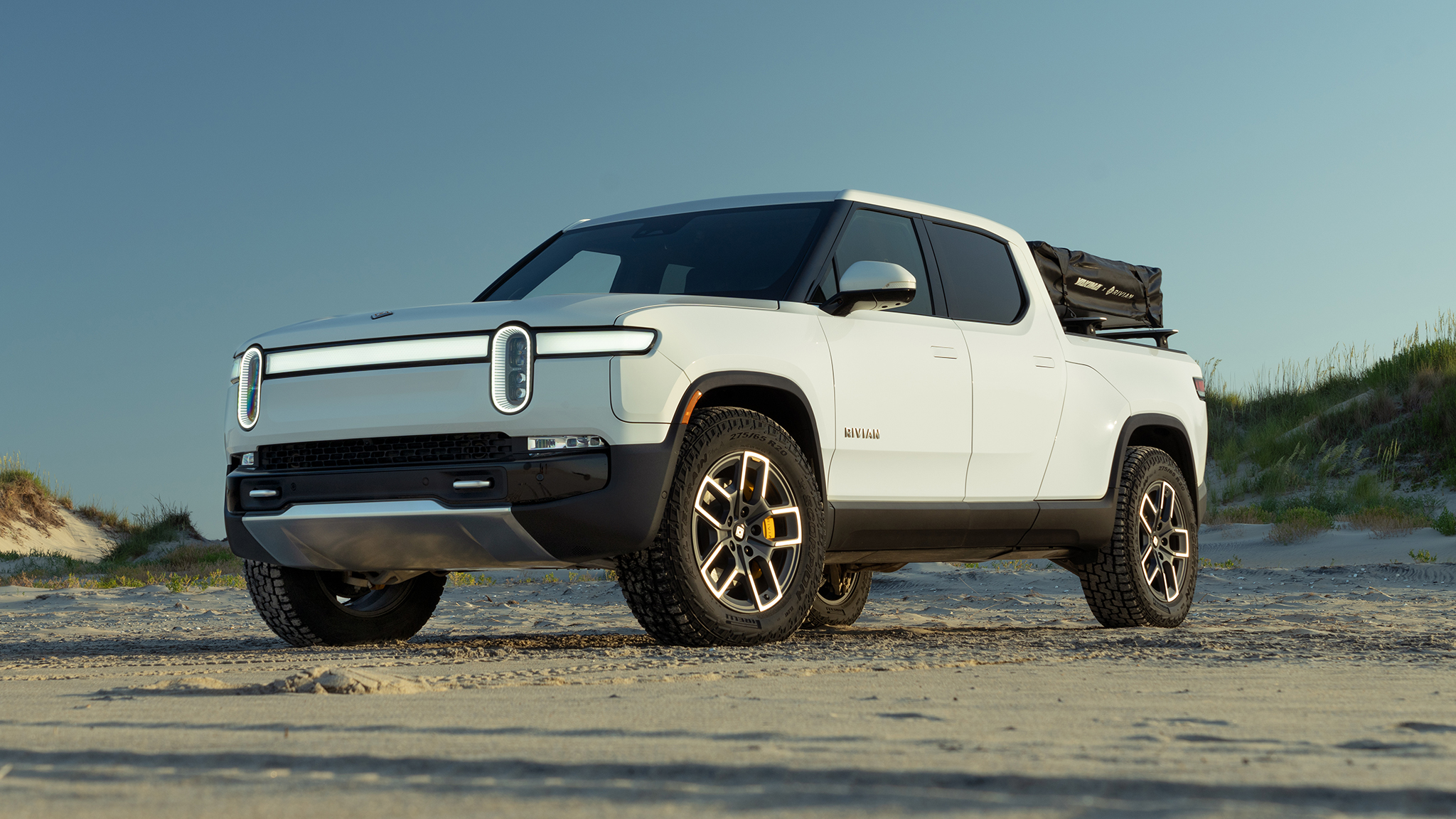 A white 2022 Rivian R1T parked in the sand on a beach