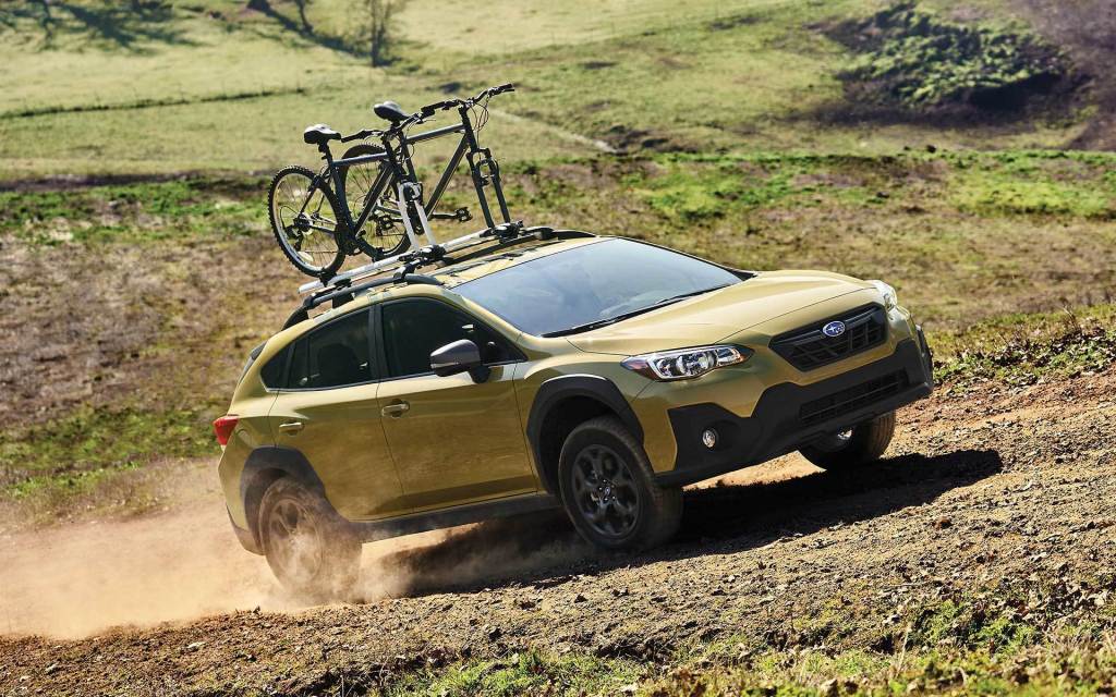 A yellow 2022 Subaru Crosstrek with a bike on top drives on a dirt road