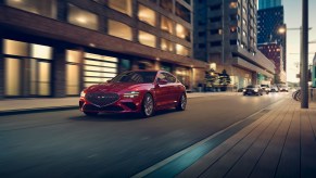 A red 2022 Genesis G70 rolling down a city street at night shot from the front 3/4