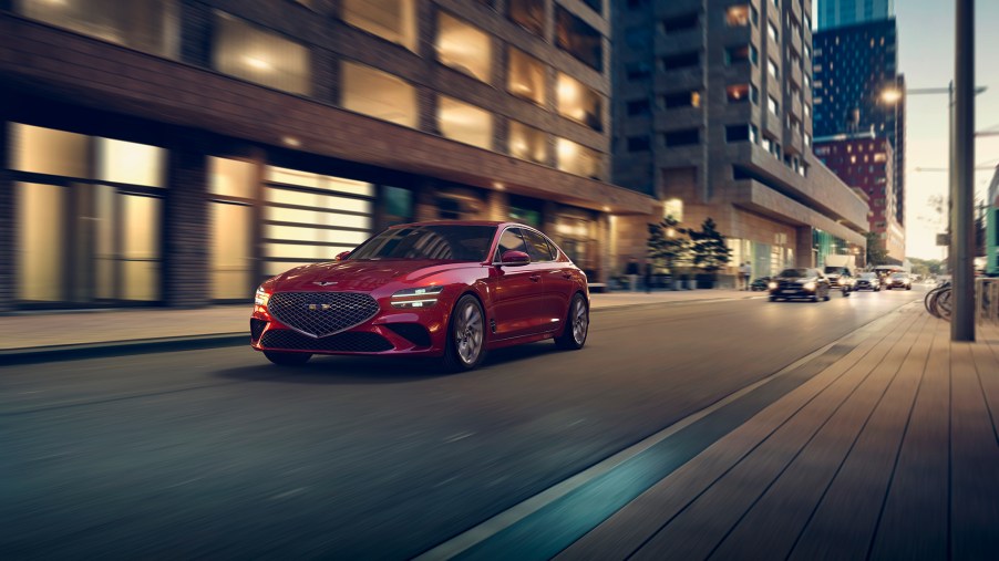 A red 2022 Genesis G70 rolling down a city street at night shot from the front 3/4