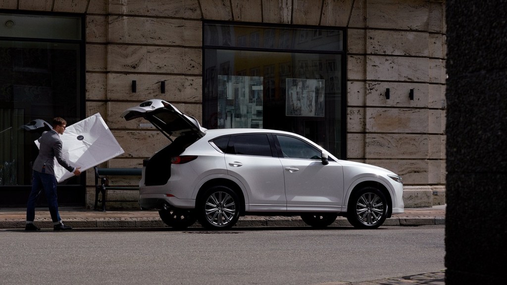 A man loading a large package into the trunk of a white 2022 Mazda CX-5.