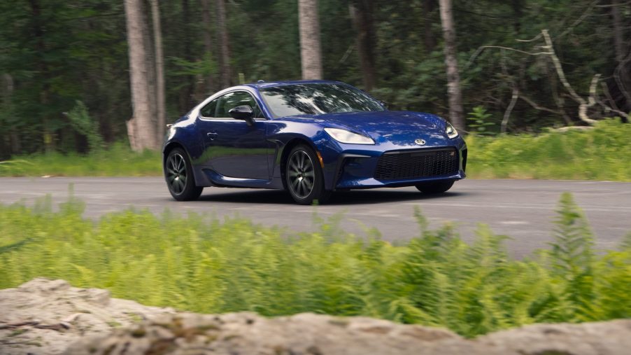 A dark blue 2022 Toyota GR 86 rolls down a forest road, shot from the front 3/4