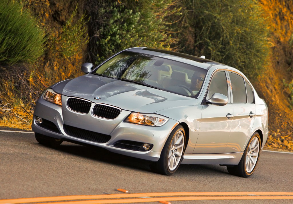 A silver 2011 BMW 3 Series sedan shot from the front 3/4 on a back road