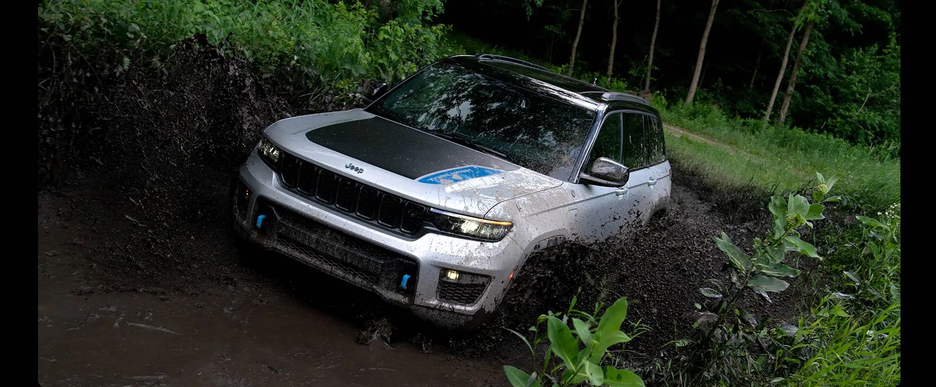 A white 2022 Jeep Grand Cherokee 4xe splashing through the mud.