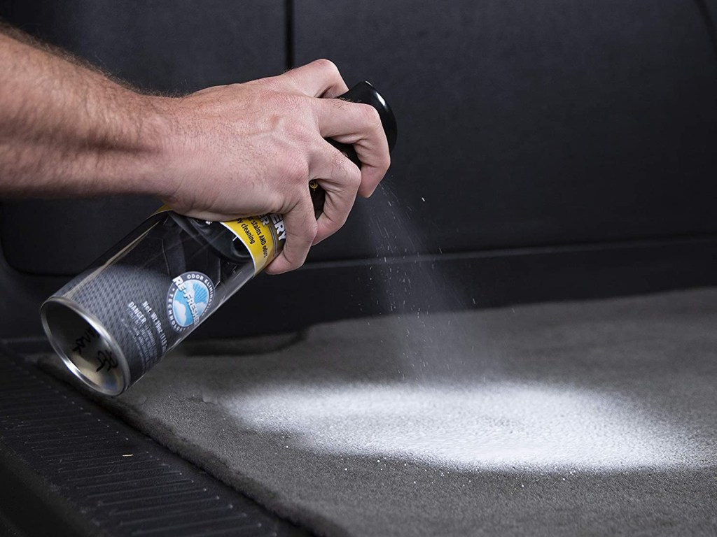 A man sprays upholstery cleaner onto a carpet, with the cleaner foaming on the mat