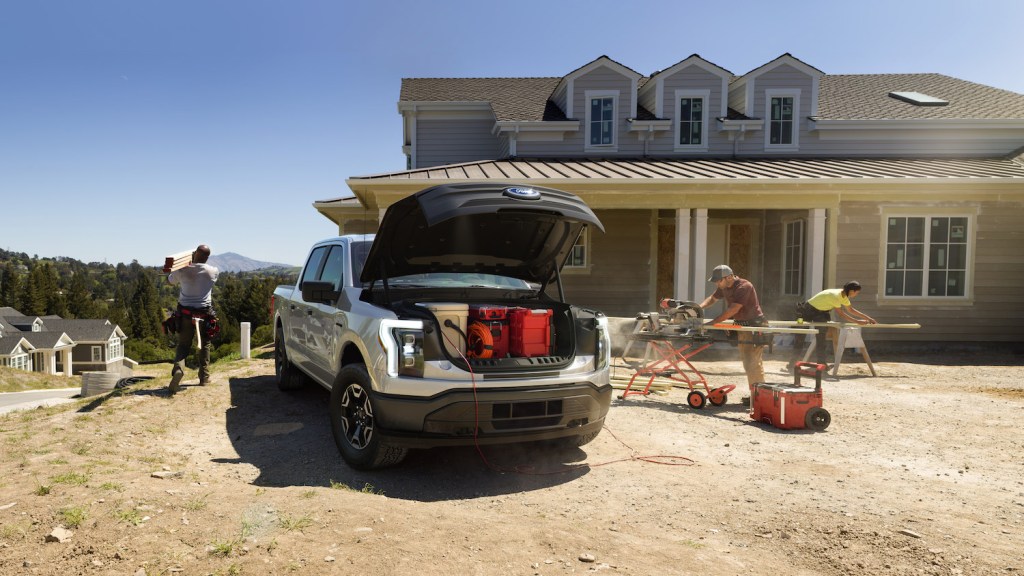 2022 Ford F-150 Lightning Pro with a front trunk open and onboard power in use. Pre-production model with available features shown. Available starting spring 2022.