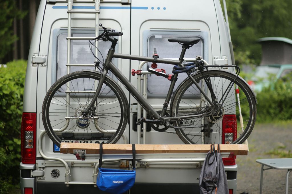 A white German RV with a gray bicycle on its ladder-mounted rack