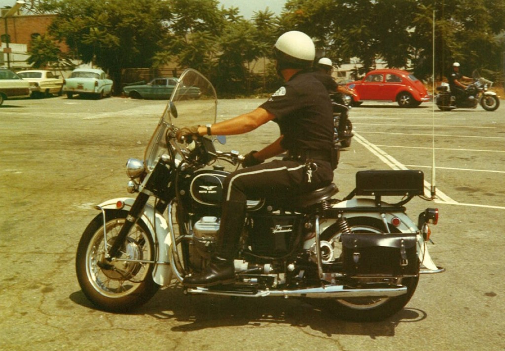 A Los Angeles police officer on a black-and-white Moto Guzzi Eldorado 850 police bike in a 1970s parking lot