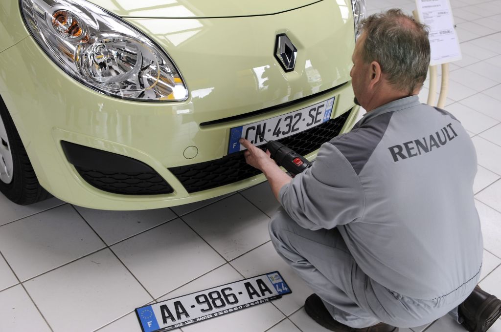 A mechanic installs a front license plate on a light-green 2009 Renault