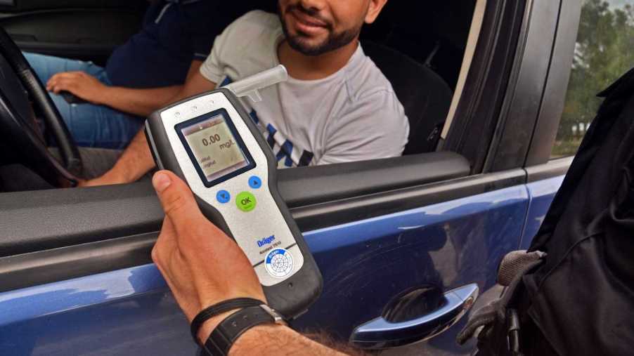 A police officer performs an alcohol breath test of a driver of a blue car