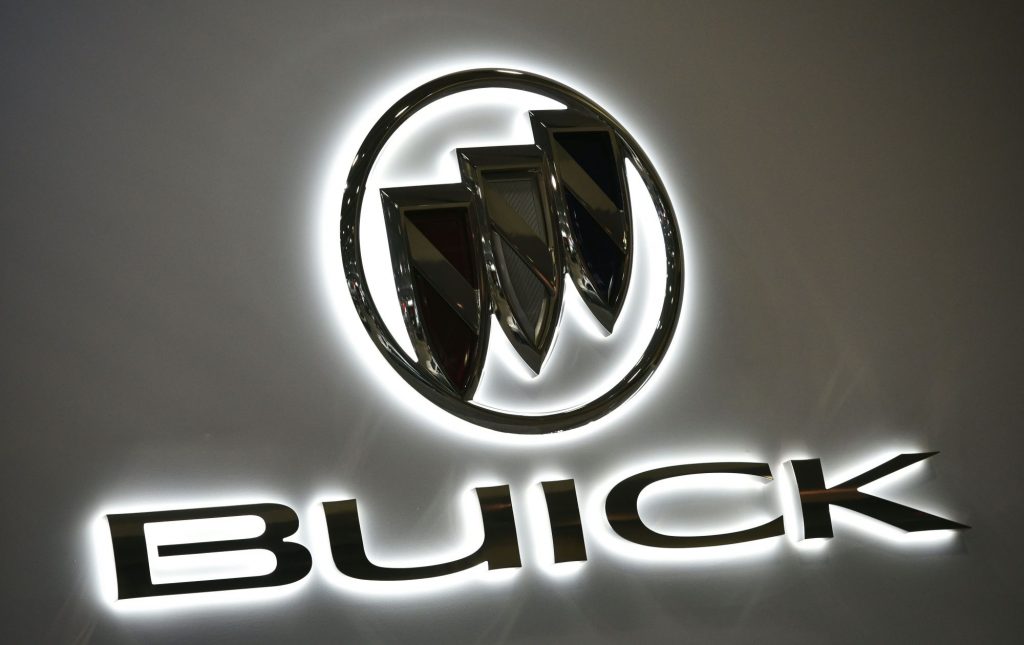 Black Buick logo with Buick printed below it on a grey background with a white light around the logo and lettering.