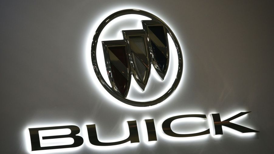Black Buick logo with Buick printed below it on a grey background with a white light around the logo and lettering.