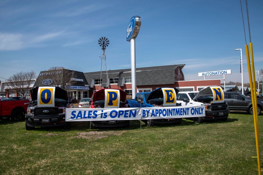 Car dealership lot with a sign that says "Open. Slaes is Open by appointment only."