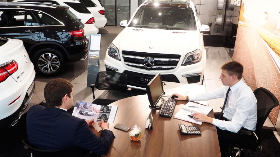 A car sales man sits with a customer at a dealership.