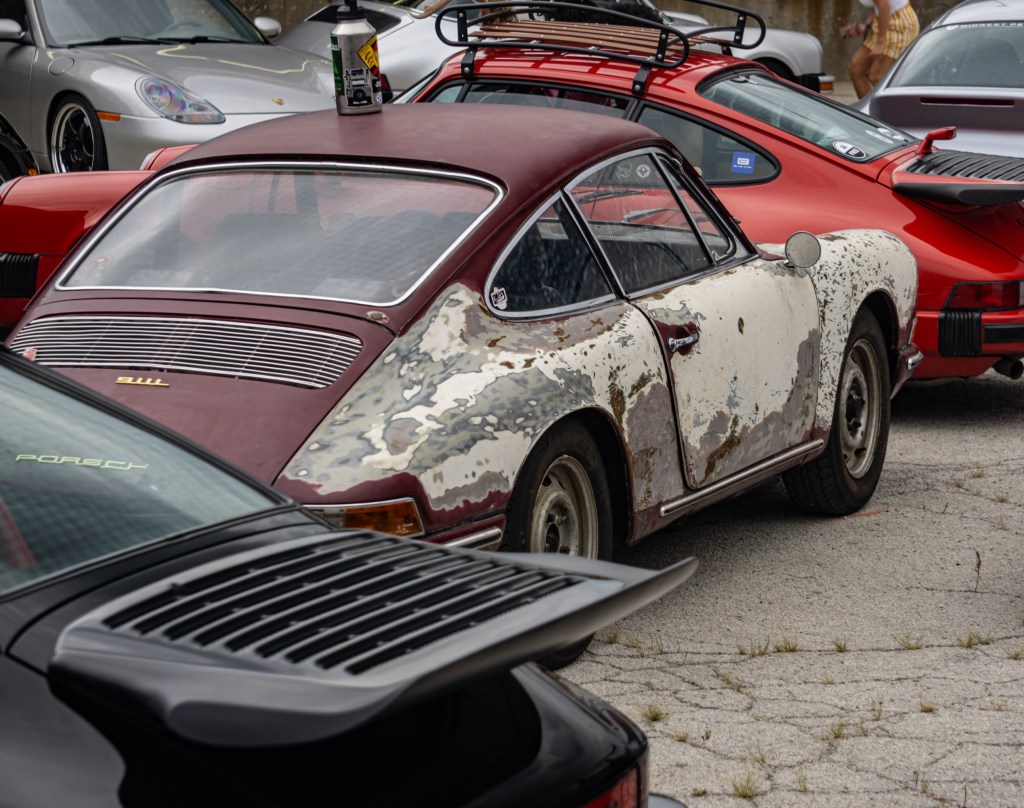 The rear 3/4 view of a classic early Porsche 911 with patina surrounded by other vintage and modern Porsches