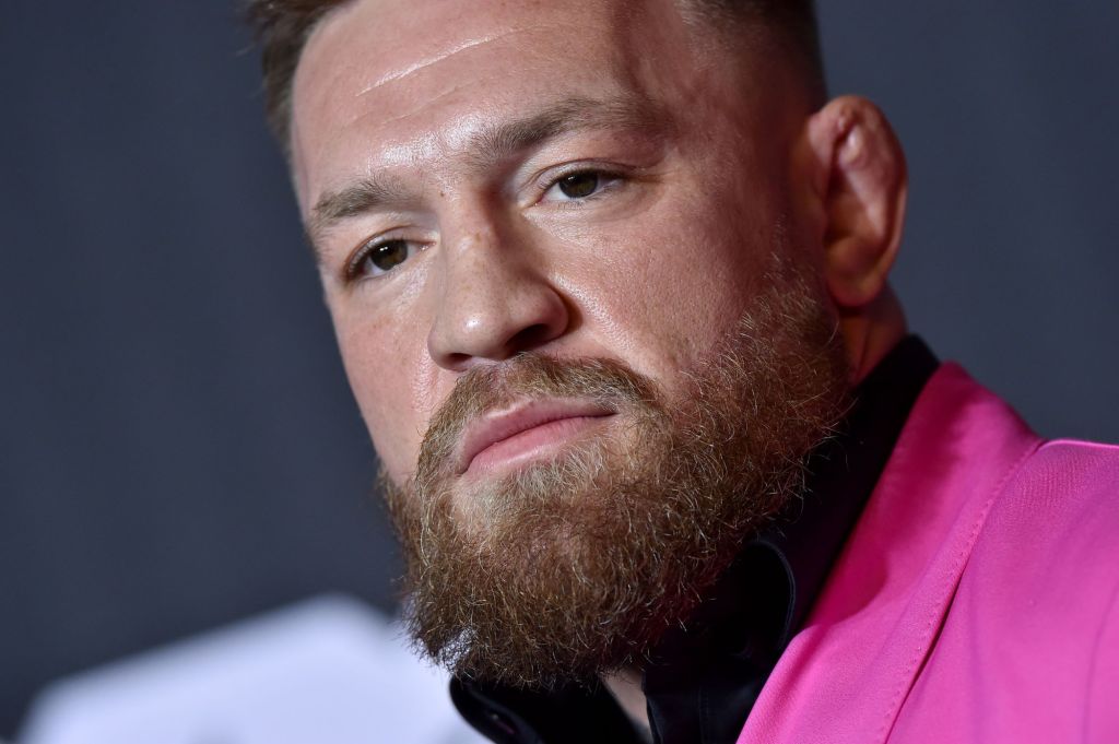 Conor McGregor in a a pink suit and black shirt in front of a grey background.