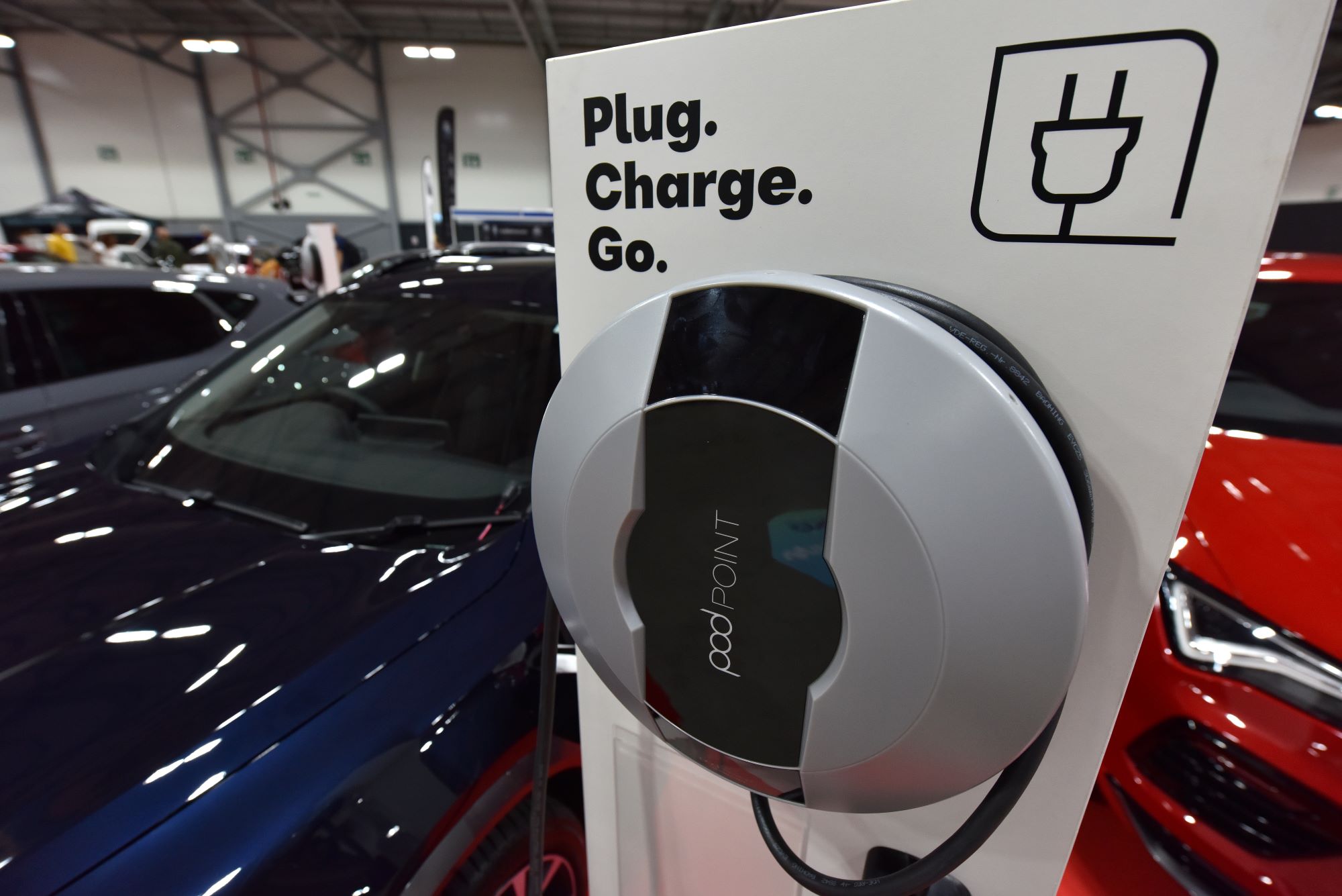 An EV charging station that says "Plug. Charge. Go." inside of a building next to a blue car.