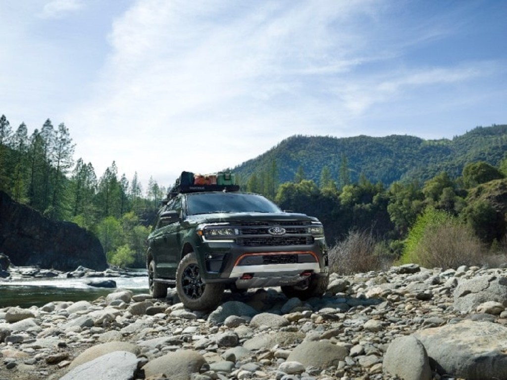 A  dark colored 2022 Ford Expedition Timberline climbs rocks next to a stream.