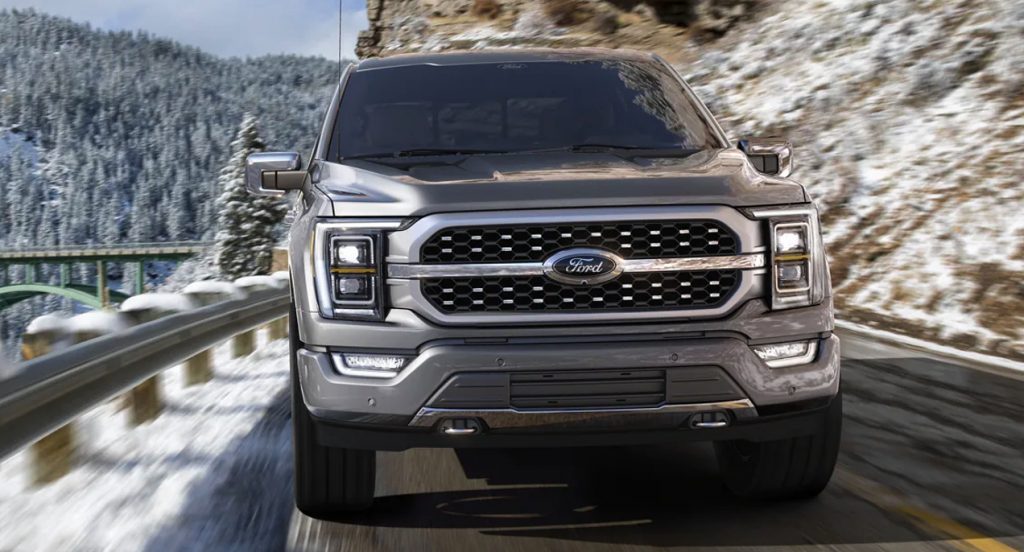 A gray Ford F-150 pickup truck is driving on a snowy road. 
