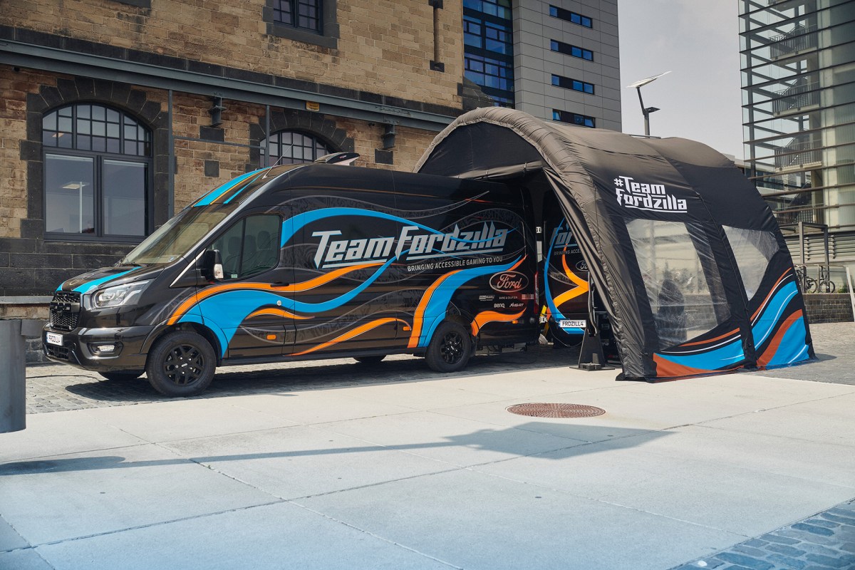 The Team Fordzilla Gaming Transit van in black with a blue and orange livery. At the rear of the van is an inflatable pop-up canopy with a similar blue and orange "wavy" livery that is featured on the van