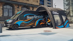 The Team Fordzilla Gaming Transit van in black with a blue and orange livery. At the rear of the van is an inflatable pop-up canopy with a similar blue and orange "wavy" livery that is featured on the van