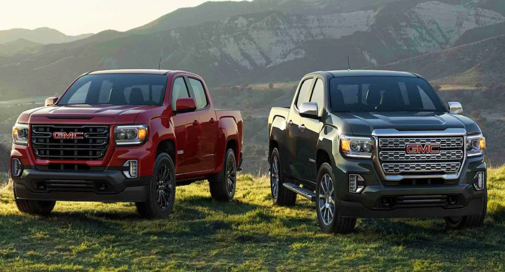 A red (left) and a black (right) GMC Canyon mid-size truck parked on a grassy plane in front of a beautiful horizon. 