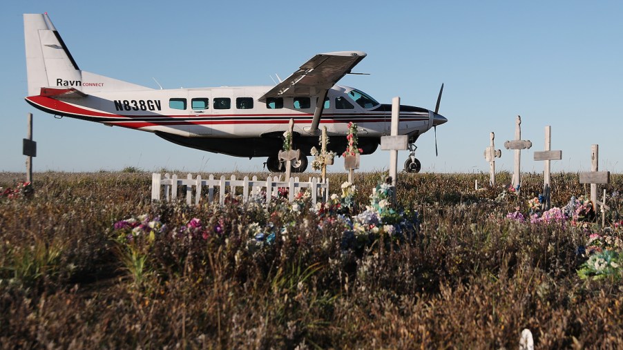 This is a commuter plane parked by a cemetery on a dirt runway in Alaska. Alaska has the highest rate of deadly plane crashes in the country.