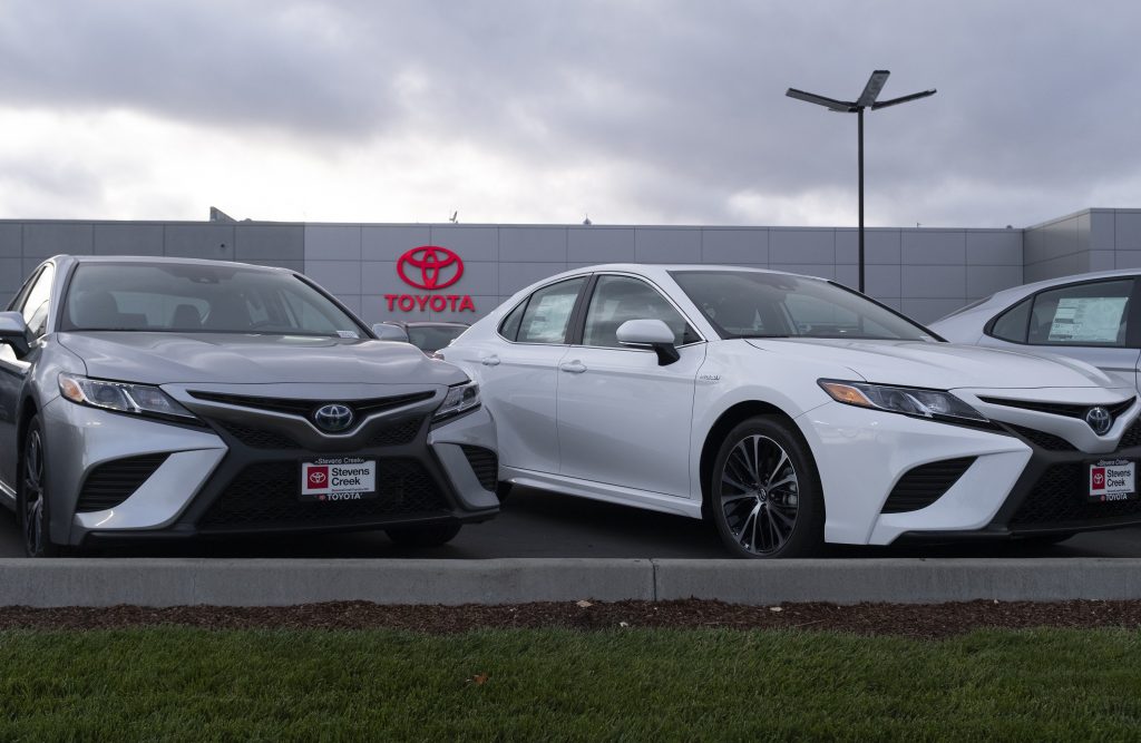 A silver and a white Toyota Camry on a dealership lot on an overcast day