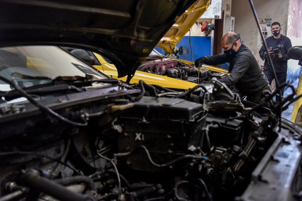 Mechanics conduct work on two cars with their hoods open. Work like this, done in a shop can be covered under an extended car warranty