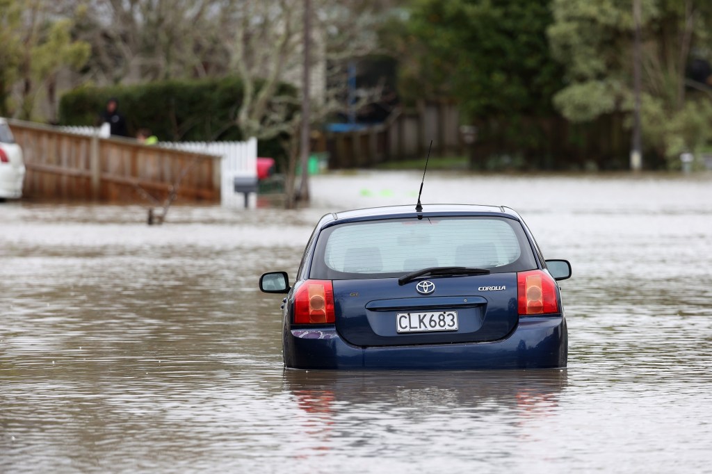 A blue Toyota Corolla wades through a flooded street in New Zealand