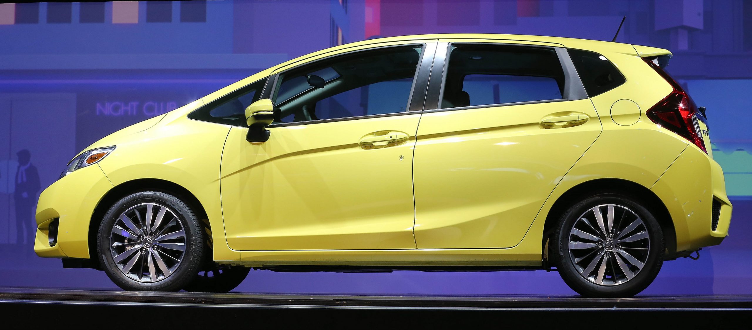 A yellow 2015 Honda Fit subcompact car shot in profile at an auto show