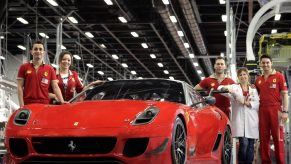 A handful of Ferrari factory workers, dressed in red, stand next to a complete Ferrari 599xx Evolution in Maranello