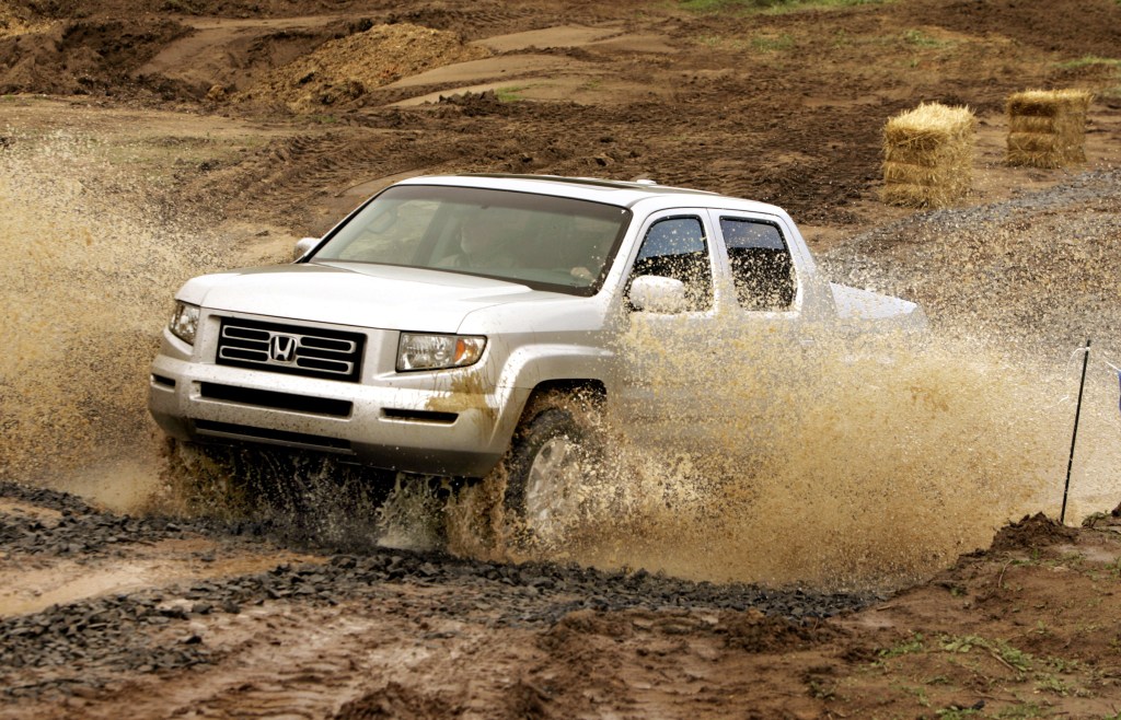 A silver Honda Ridgeline pickup truck is off-roading in the mud. 