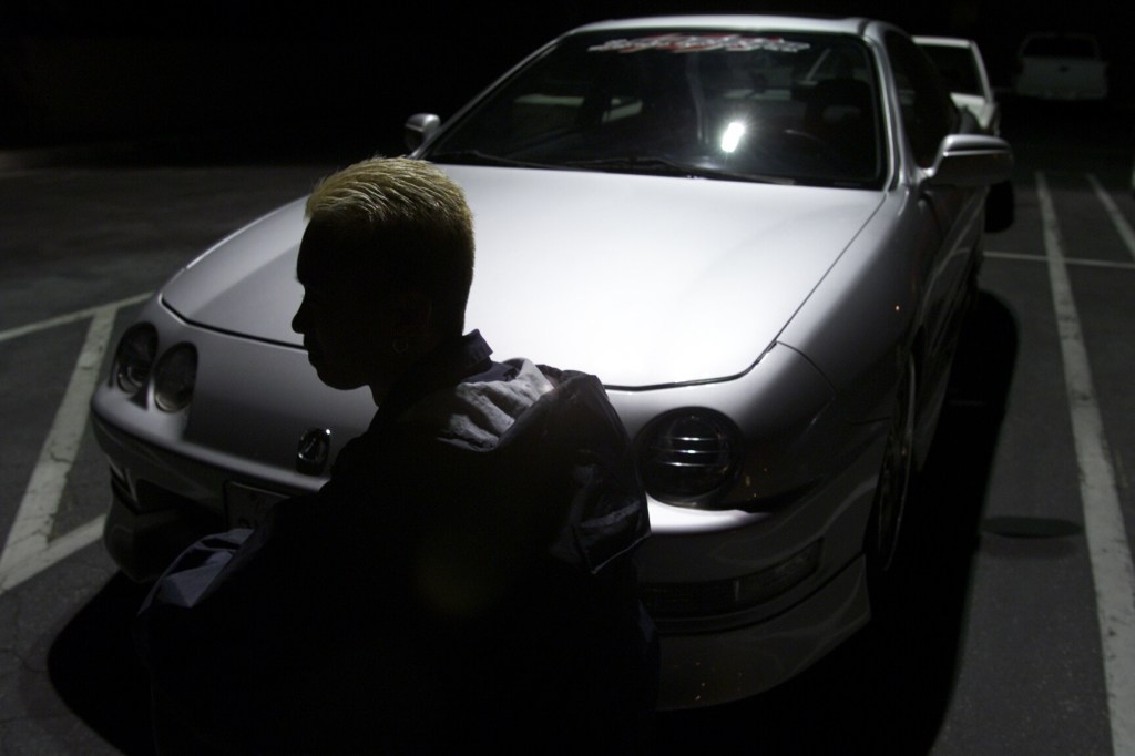 A man sits in the shadows in front of a first-generation Acura Integra