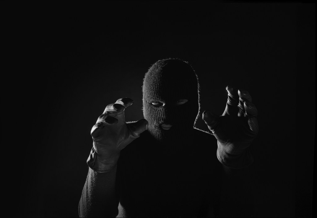 A man in a balaclava raises his gloved hands towards the camera