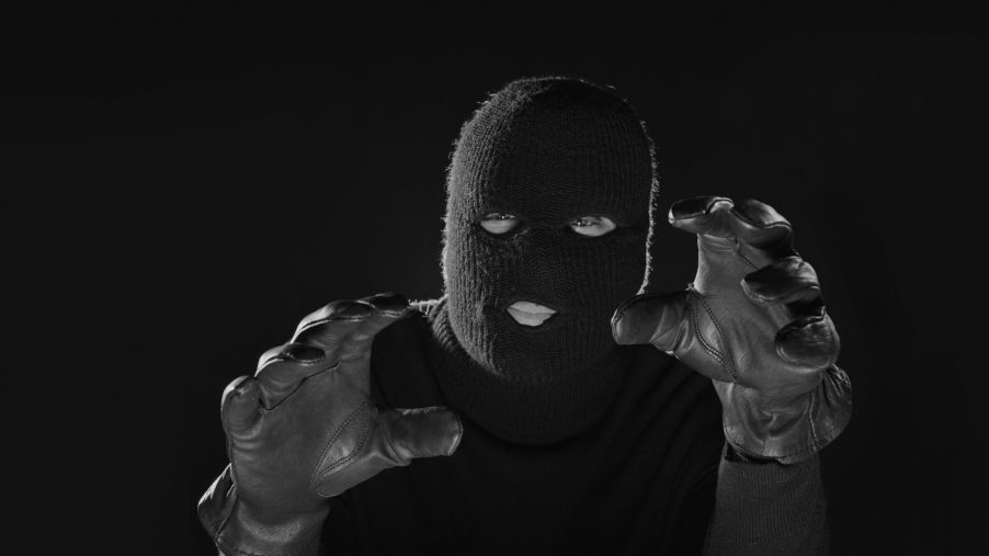 A man in a balaclava raises his gloved hands towards the camera