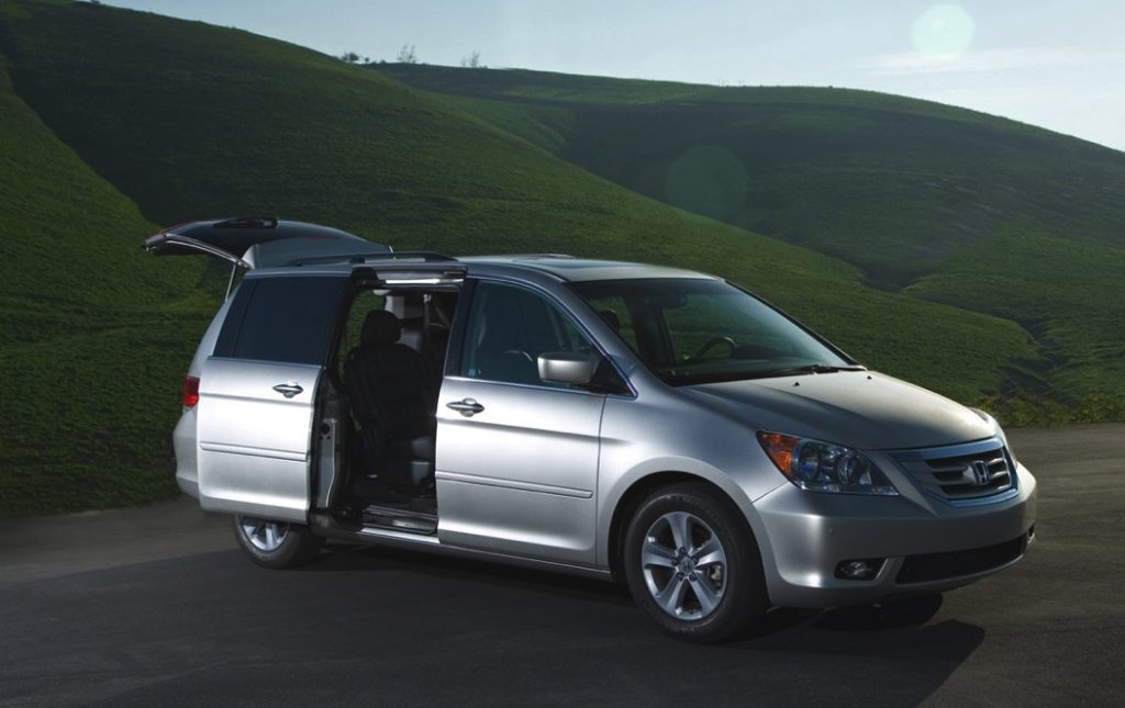 A honda odyssey is parked near a grassy hill at night with the doors open