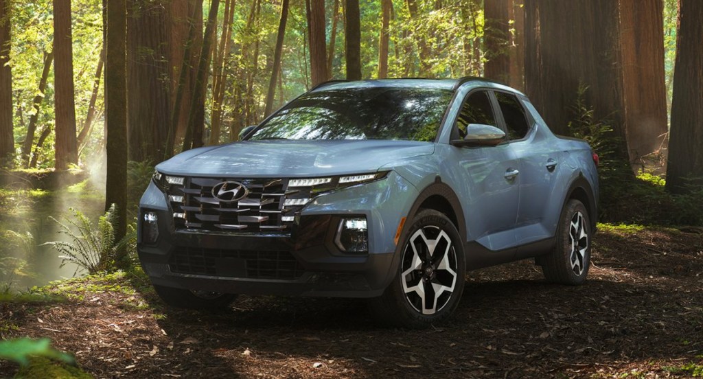 A blue Hyundai Santa Cruz small pickup truck is parked in the forest. 