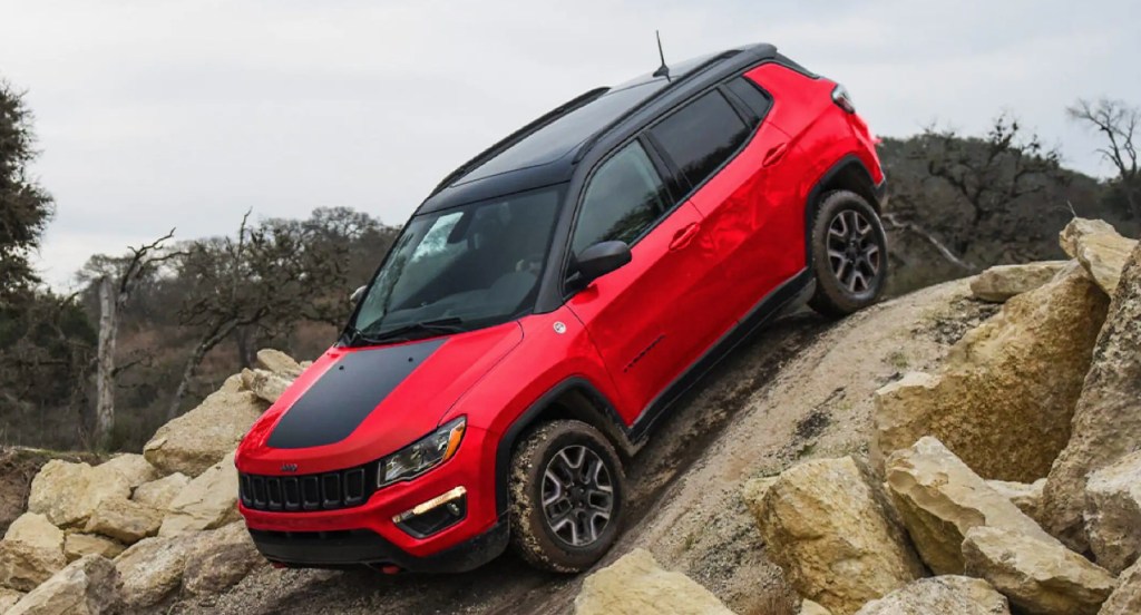 A red Jeep Compass Trailhawk package is descending down a hill surrounded by rocks. 