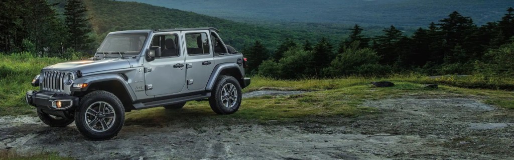 A light gray Jeep Wrangler parked in the mountains.