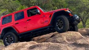 A red Jeep Wrangler small off-road SUV is climbing rocks.