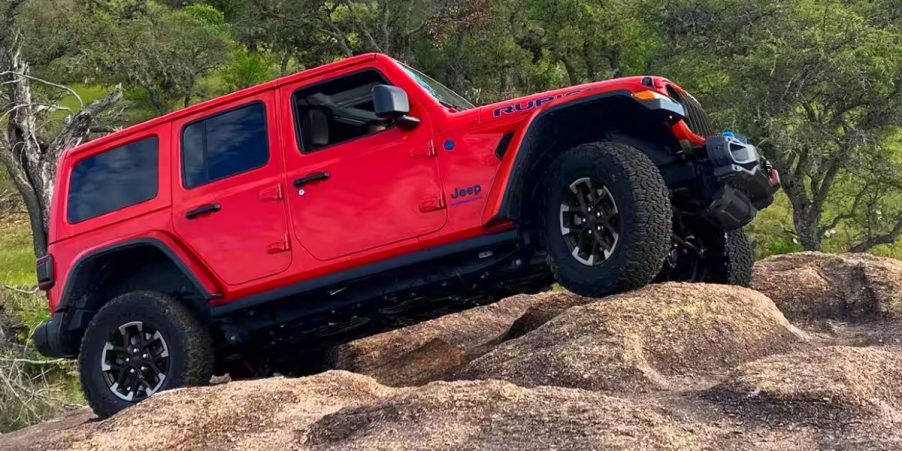 A red Jeep Wrangler small off-road SUV is climbing rocks.