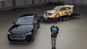 Ken Block standing next to an Audi e-tron SUV with an Audi S1 Quattro rally car on a trailer. Ken Block will pilot an Audi EV in a future “Electrikhana” video