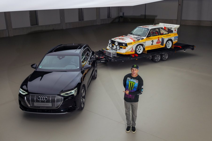 Ken Block standing next to an Audi e-tron SUV with an Audi S1 Quattro rally car on a trailer. Ken Block will pilot an Audi EV in a future “Electrikhana” video