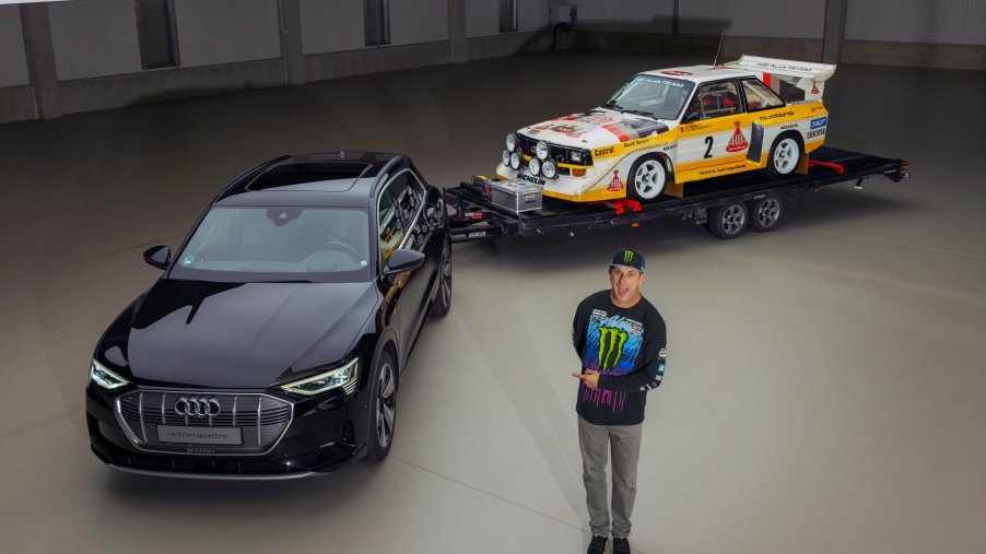 Ken Block standing next to an Audi e-tron SUV with an Audi S1 Quattro rally car on a trailer. Ken Block will pilot an Audi EV in a future “Electrikhana” video