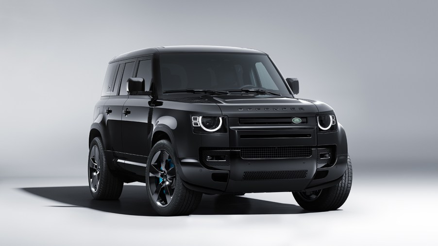 Land Rover Defender V8 Bond Edition in all black. Photo shot in a white studio. Vehicle is facing the camera with the front wheels slightly turned to the viewer's right, revealing a hint of the blue brake calipers.
