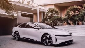 A white Lucid Air in front of a modern style home with palm trees.
