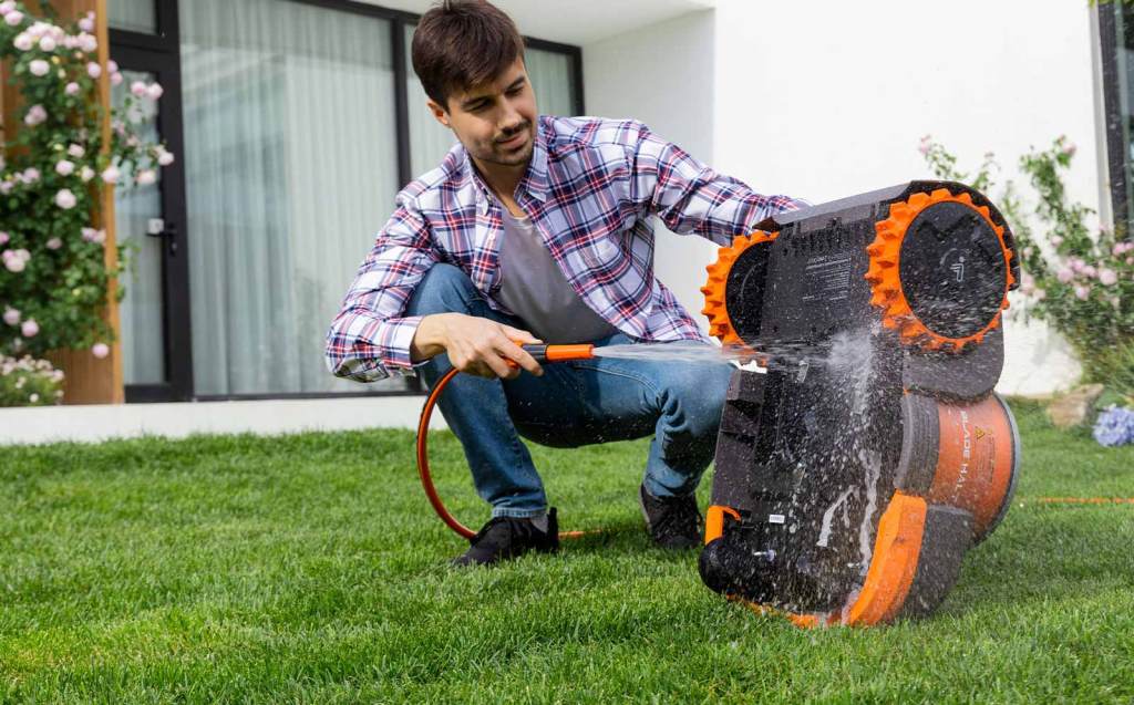 A man washes a Segway Navimow with a hose in the middle of his lawn
