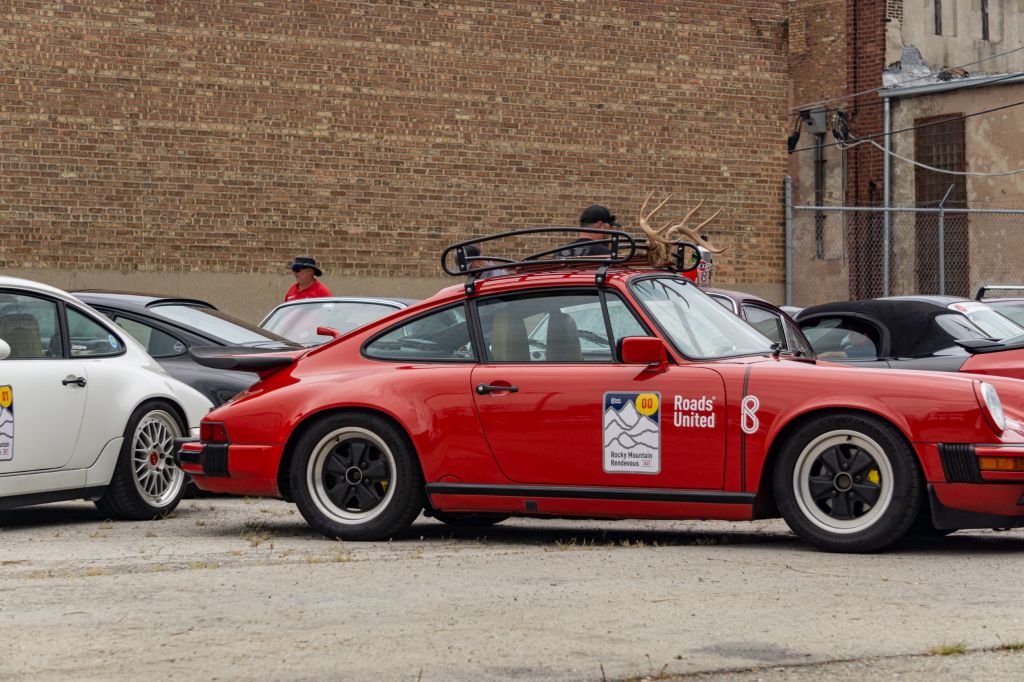 The side view of a modified red 1987 Porsche 911 Carrera 3.2 in a parking lot amongst other Porsche cars