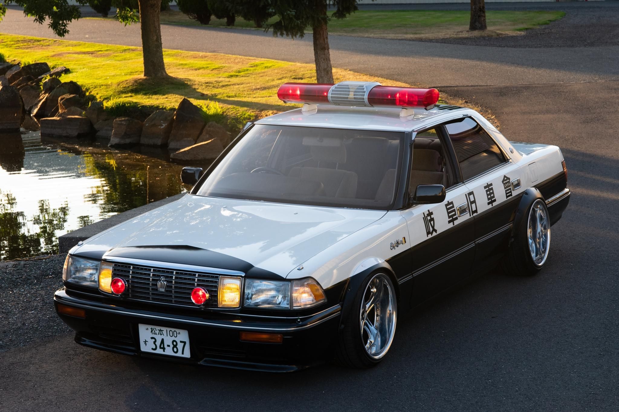 A 1991 Toyota modified to resemble a black-and-white Japanese police car parked next to a pond